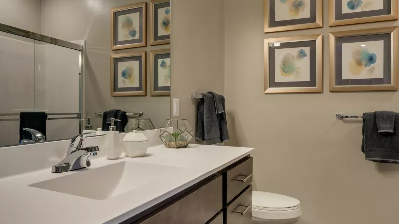 Modern bathroom with a dark wood vanity, white counter, large mirror, and four framed abstract art prints.