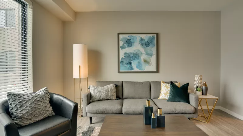Photograph of a modern living room with a grey sofa, dark armchair, wooden coffee table, and blue abstract art.
