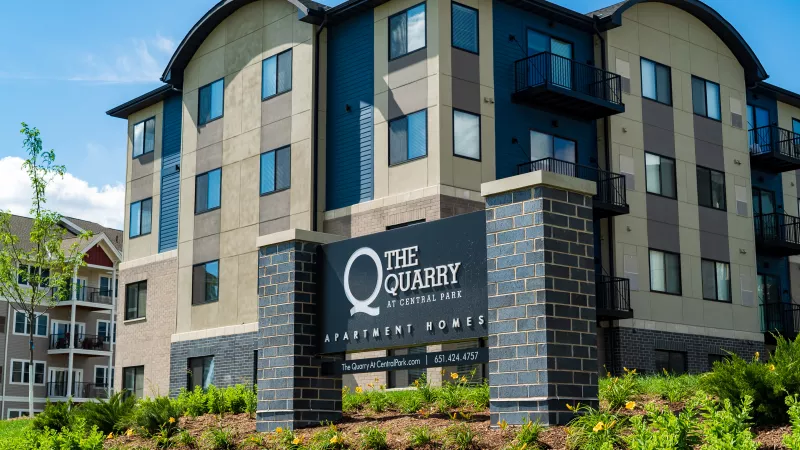 Modern "The Quarry at Columbia Road" apartment building with blue, grey, and tan siding, and a prominent dark brick sign.