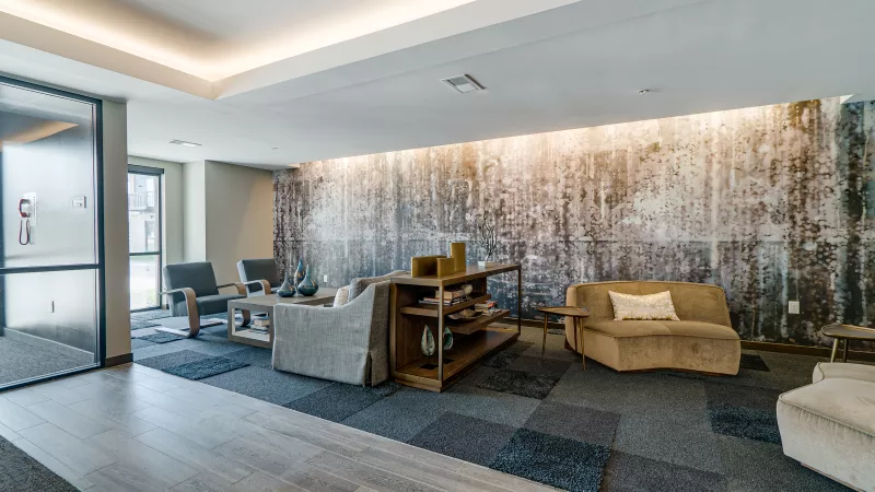 Modern lounge area with a forest mural, beige sofas, and patterned carpet. Warm lighting illuminates the space.