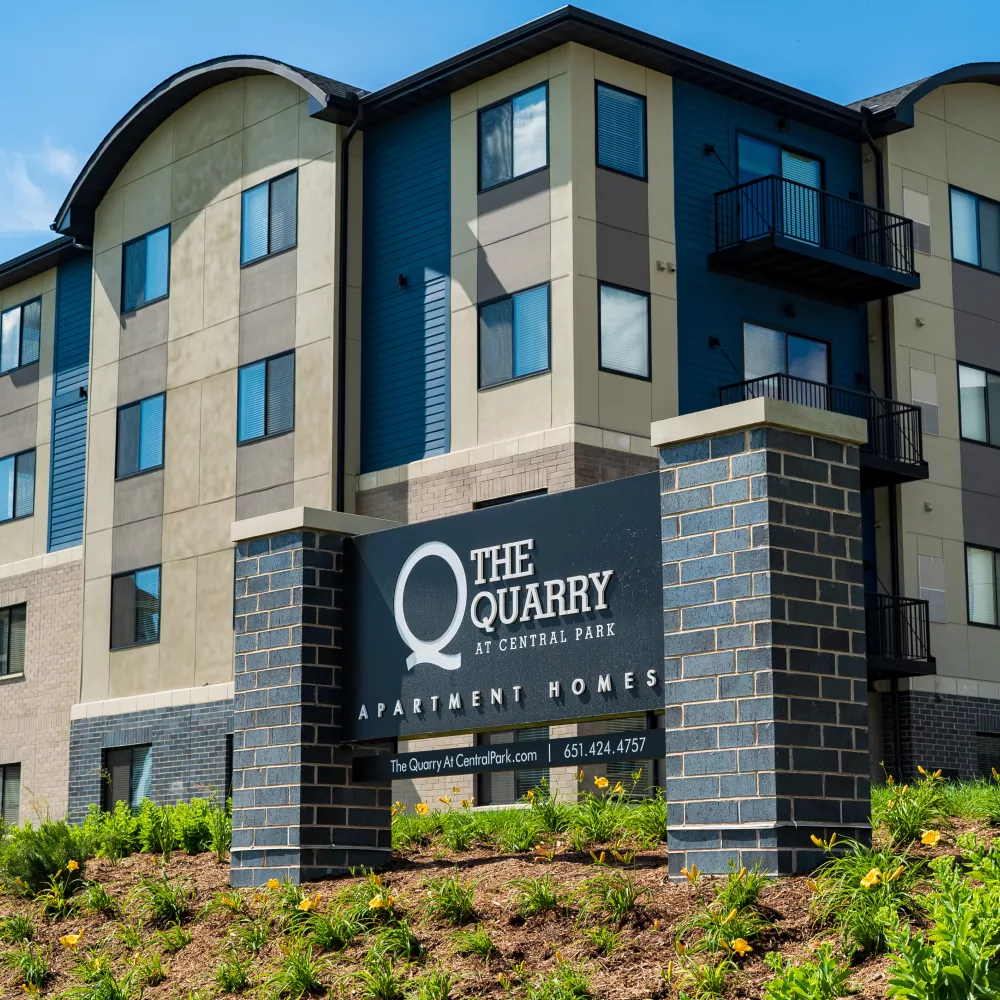 Modern "The Quarry at Columbia Road" apartment building with blue, grey, and tan siding, and a prominent dark brick sign.