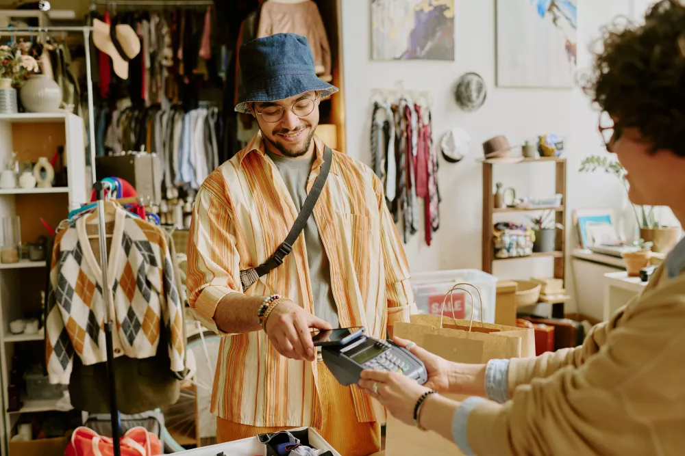 Smiling man in a bucket hat paying a cashier with a credit card in a vibrant clothing store.