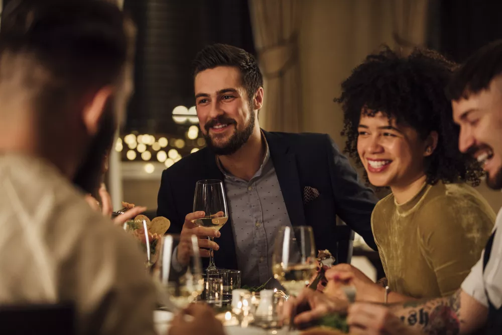 Smiling friends share a meal and wine at a festive, elegant dinner party.